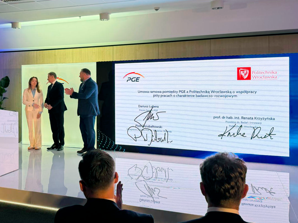 Zdjęcie dokumentuje oficjalne zawarcie umowy ramowej, która inicjuje strategiczną współpracę pomiędzy grupą energetyczną PGE a Politechniką Wrocławską. Przedstawione na ekranie podpisy kluczowych przedstawicieli obu stron potwierdzają wolę wspólnego realizowania projektów o charakterze badawczo-rozwojowym. Wydarzenie to podkreśla istotne dążenie do integracji świata nauki z przemysłem, co ma na celu wdrażanie nowoczesnych rozwiązań technologicznych w sektorze energetycznym. Całość kompozycji wskazuje na formalny i prestiżowy charakter partnerstwa, nakierowanego na stymulowanie innowacji oraz rozwój kadr naukowych.